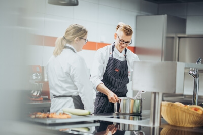 Zwei Koch-Auszubildende bereiten eine Sauce vor.