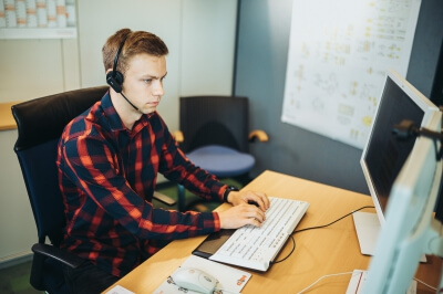 Auszubildender Fachinformatiker für Systemintegration mit Headset arbeitet konzentriert am PC.