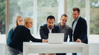 Besonders in Projekten ist Team-Arbeit Trumpf. Mehrere LBS NordWest Mitarbeiter stehen um einen Laptop.