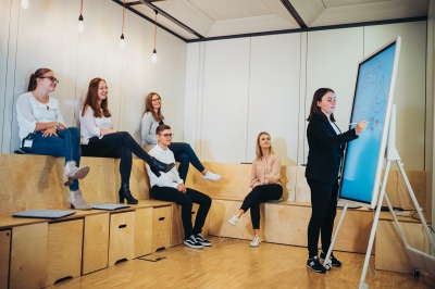 LBS Auszubildende sitzen zusammen und schauen gemeinsam auf ein Smartboard, welches von einer Auszubildenden beschriftet wird.