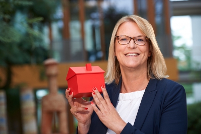 LBS Kollegin lächelt mit einem roten Haus in ihrer Hand in die Kamera im LBS Gebäude in Hannover