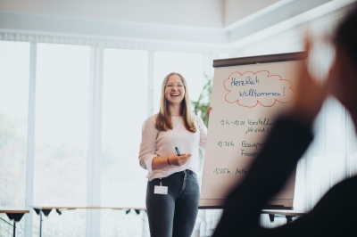 Junge LBS Kollegin lächelt beim Präsentieren von Inhalten an einem Flipchart