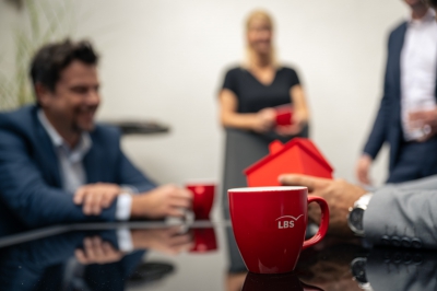 LBS-Beraterinnen und Berater stehen mit LBS-Kaffeetassen um einen Tisch herum.